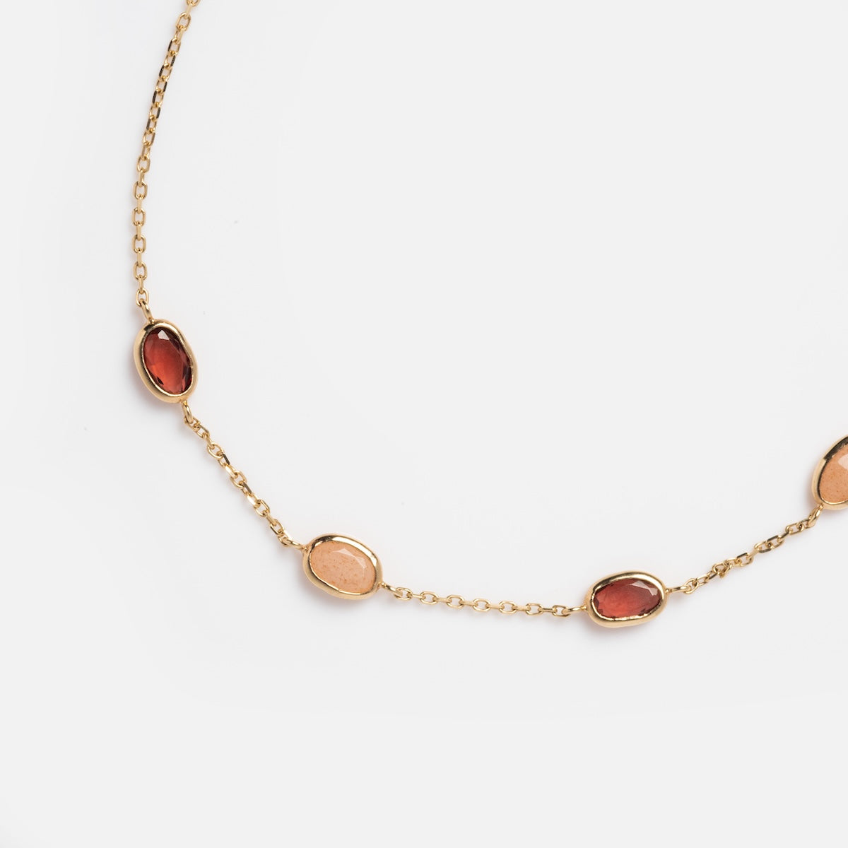 The Solid Gold Sunlit Garnet and Sunstone Bracelet features oval garnet and sunstone gemstones in peach and rust tones, evenly spaced along a delicate gold chain, displayed on a white background.