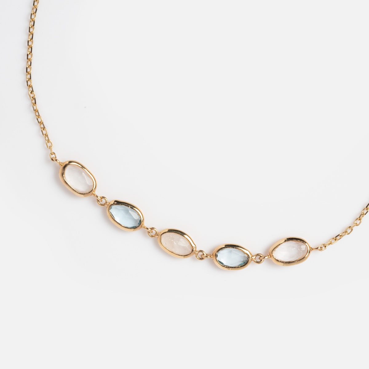 A gold necklace with oval stones, capturing the elegance of the Solid Gold Daybreak Moonstone and Blue Topaz Bracelet.