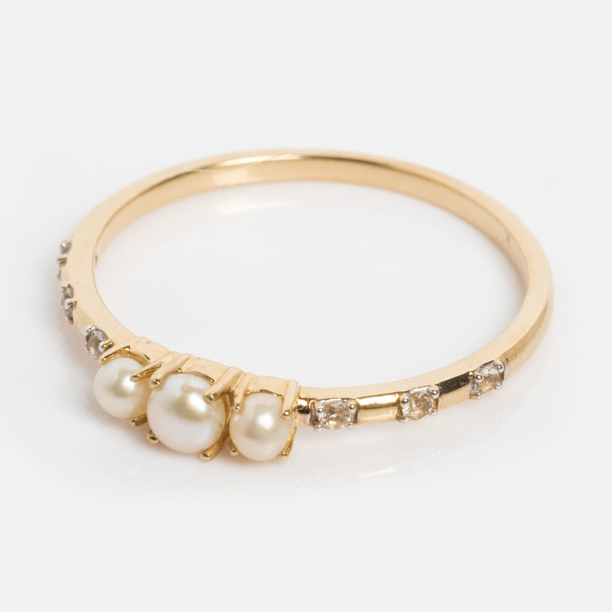 The Solid Gold Luminous Pearl Trio Ring showcases three white pearls at the center, accented by round diamonds along both sides of the band, set against a white background.