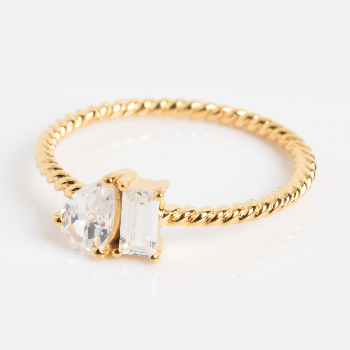 The Twisted Toi Et Moi Ring features a gold twisted band with two prong-set gemstones—one round and one rectangular—side by side, displayed against a plain white background.