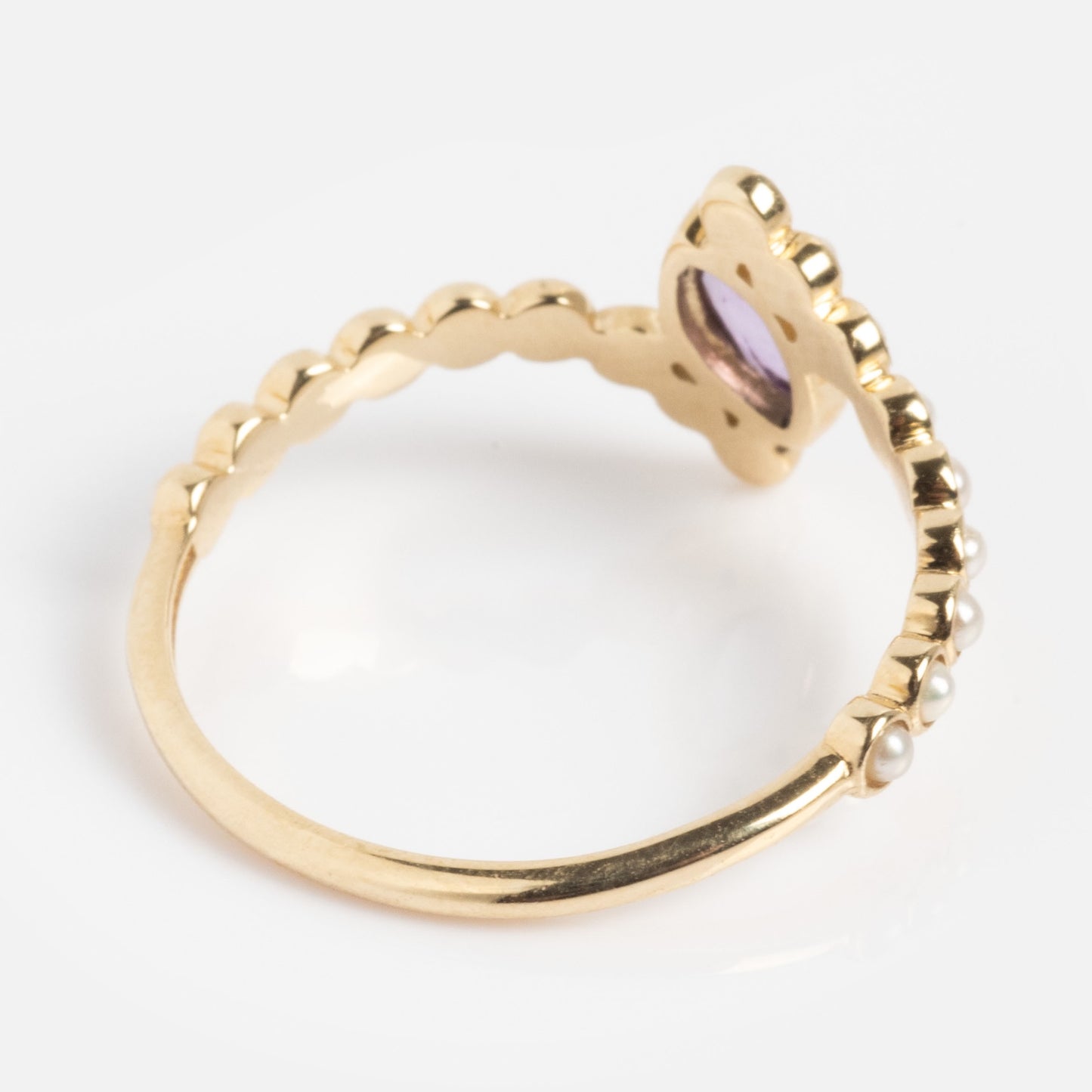 The Solid Gold 2026 February Capsule Floating Amethyst and Pearl Twist Ring features a scalloped gold band, small pearls on one side, and a flower-shaped setting with a light purple amethyst. Photographed on a white background.