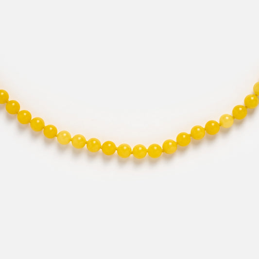 A close-up of the Beaded Gemstone Necklace shows its yellow beads and 18k gold plated accents, elegantly arranged in a gentle curve against a white background.