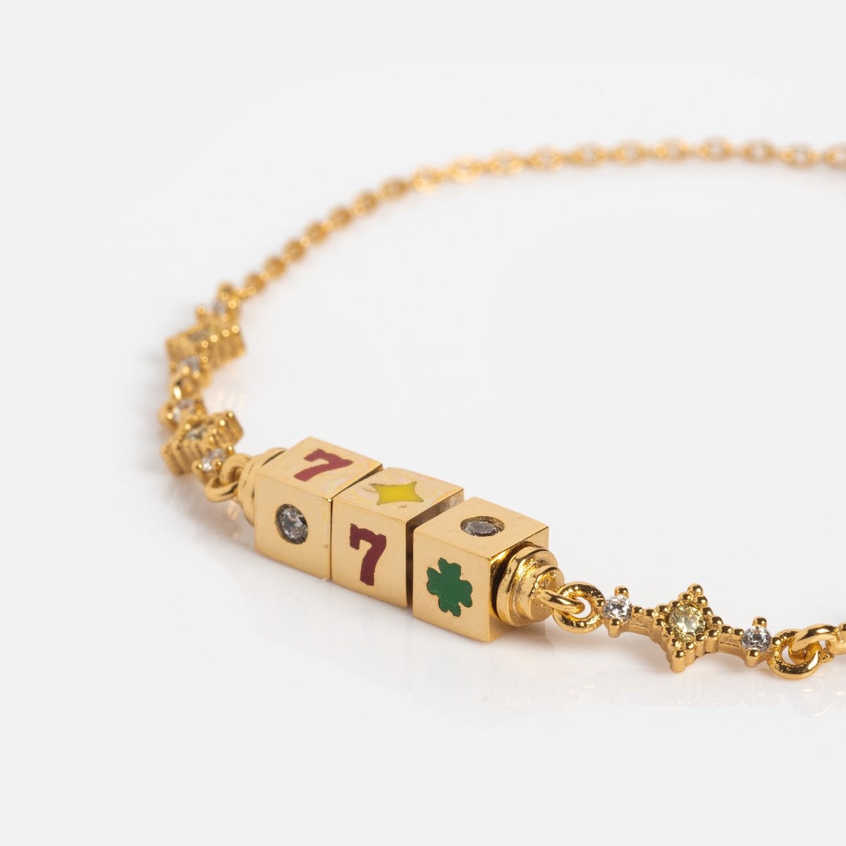 The Hit The Jackpot Bracelet is an 18k yellow gold plated chain with three cube-shaped beads featuring a red 7, yellow star, green clover, clear gem, sparkling stones, and small star-shaped links.