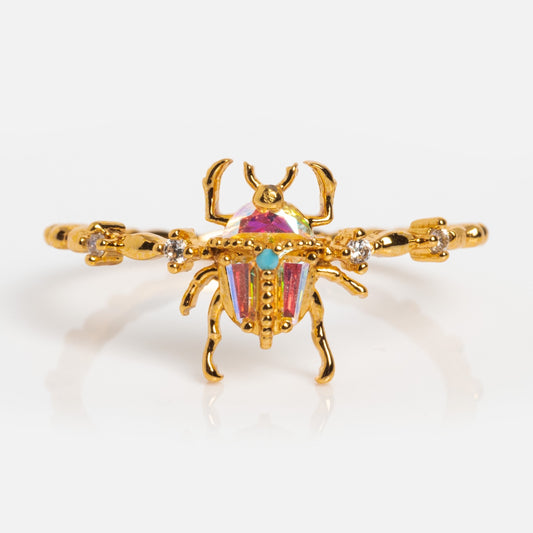 The Beetlejuice Ring features a beetle-shaped design in 18k yellow gold-plated metal with colorful iridescent CZ stones and gemstone accents, displayed against a white background.