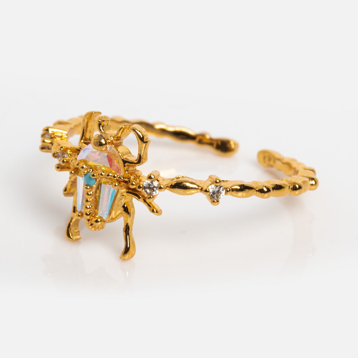 The Beetlejuice Ring features a beetle-shaped ornament with an iridescent CZ stone body on an 18k yellow gold plated band accented with small clear stones, displayed on a white background.