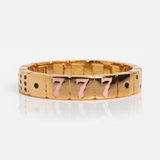 The 777 Ring is a gold-plated piece with pink enamel 777 and black dots in groups, creating a slot machine or dice-inspired design on a white background.