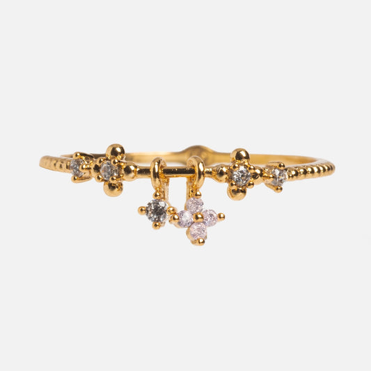 The Charmed Blossom Ring features delicate 18k yellow gold plating, CZ stones, a central flower charm with pink and white accents, two dangling charms, and a beaded milgrain band.