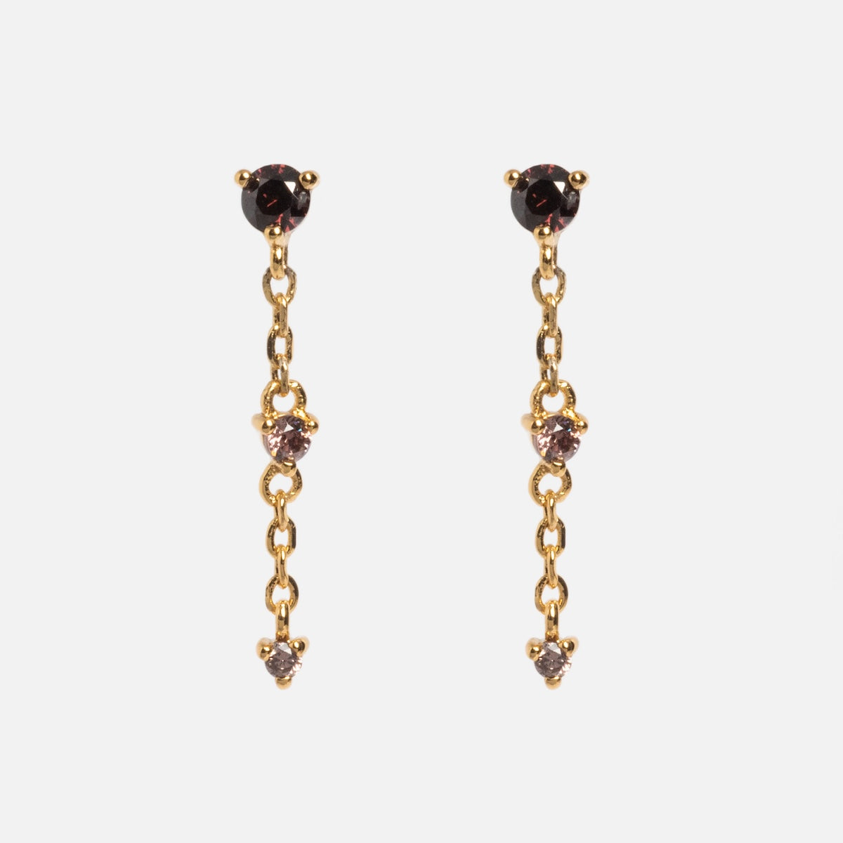 The Celebration Ombre Birthstone Drop Studs are 14k gold plated earrings with a short chain, featuring a small round dark gemstone at the top and two smaller clear stones spaced along the hanging chain, shown on a white background.