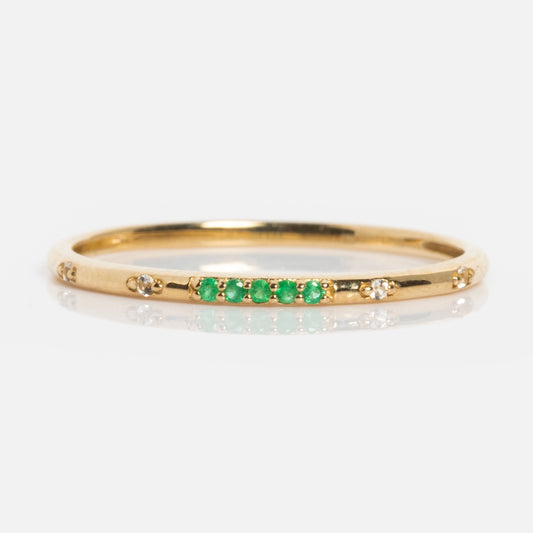 The Solid Gold 2025 May Capsule Emerald Ring features five green stones in a row and white accents along the band. Ideal as May birthstone jewelry, it comes with a free gift and is displayed on a white background.