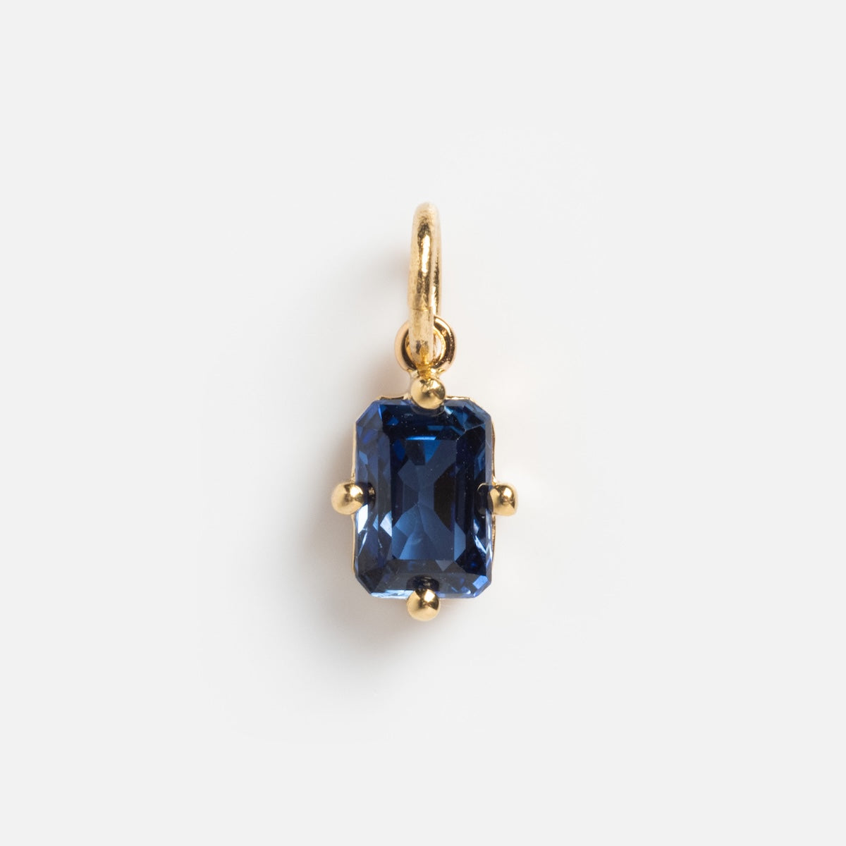 The 14k Mod Love Birthstone Charm is a gold pendant with an emerald-cut deep blue gemstone baguette, secured by four gold prongs and attached to a small gold loop, shown on a plain white background.