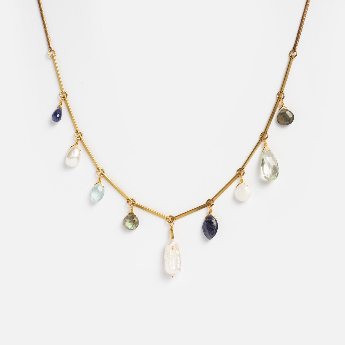 The Oceana Necklace Sample features a gold chain with multiple dangling charms—green amethyst, labradorite, moonstone gemstones in varied shapes and colors—and a central irregular white pearl, displayed against a white background.