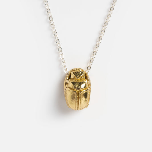 The Scarab Pendant hangs from a sterling silver chain necklace, showcased against a plain white background.