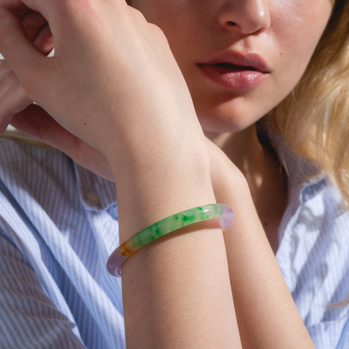 A woman in a striped blue shirt poses with her hand near her face, showcasing the Lavender Field Multicolor Quartzite Bangle—true wearable art with green and yellow accents—on her wrist.