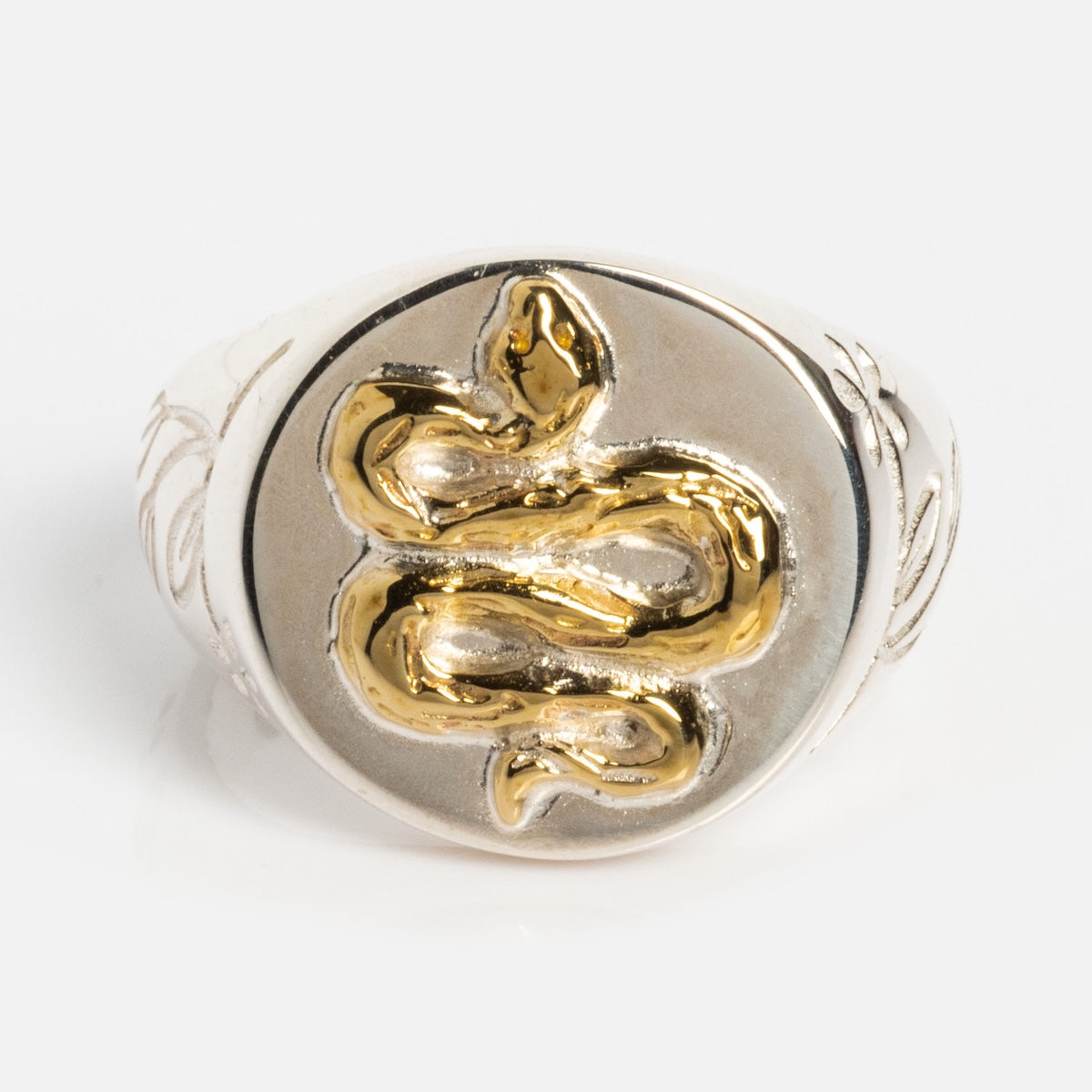 The Serpent Signet Ring is a sterling silver piece with a raised gold vermeil serpent coiled at the center and subtle floral engravings on the sides, shown on a plain white background.