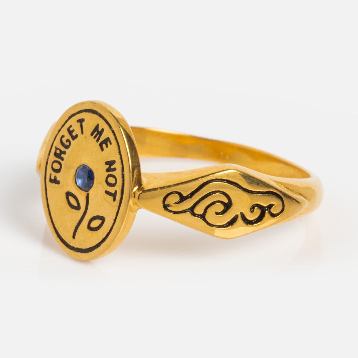 The Forget Me Not Ring is a yellow gold vermeil signet ring with an engraved round face that reads FORGET ME NOT, featuring a central blue sapphire in a floral design and an ornate wave pattern on the band.