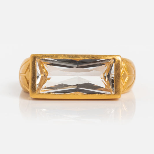The Eternal Radiance White Topaz Ring is gold plated with a large, rectangular white topaz in a horizontal setting. Its band features subtle geometric patterns and a polished finish, beautifully photographed on a white background.