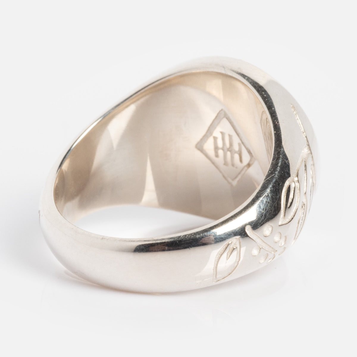 The Serpent Signet Ring, crafted in sterling silver, features engraved leaves and berries on the outside and a diamond-shaped hallmark inside, shown against a white background.