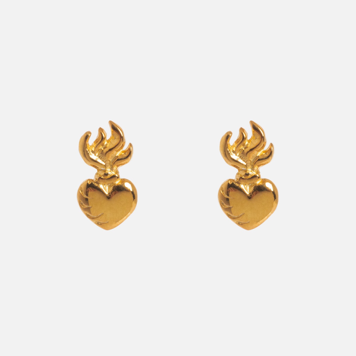 The Sacred Heart Stud Earrings are gold vermeil heart-shaped earrings with flame-like designs at the top, shown against a plain white background.