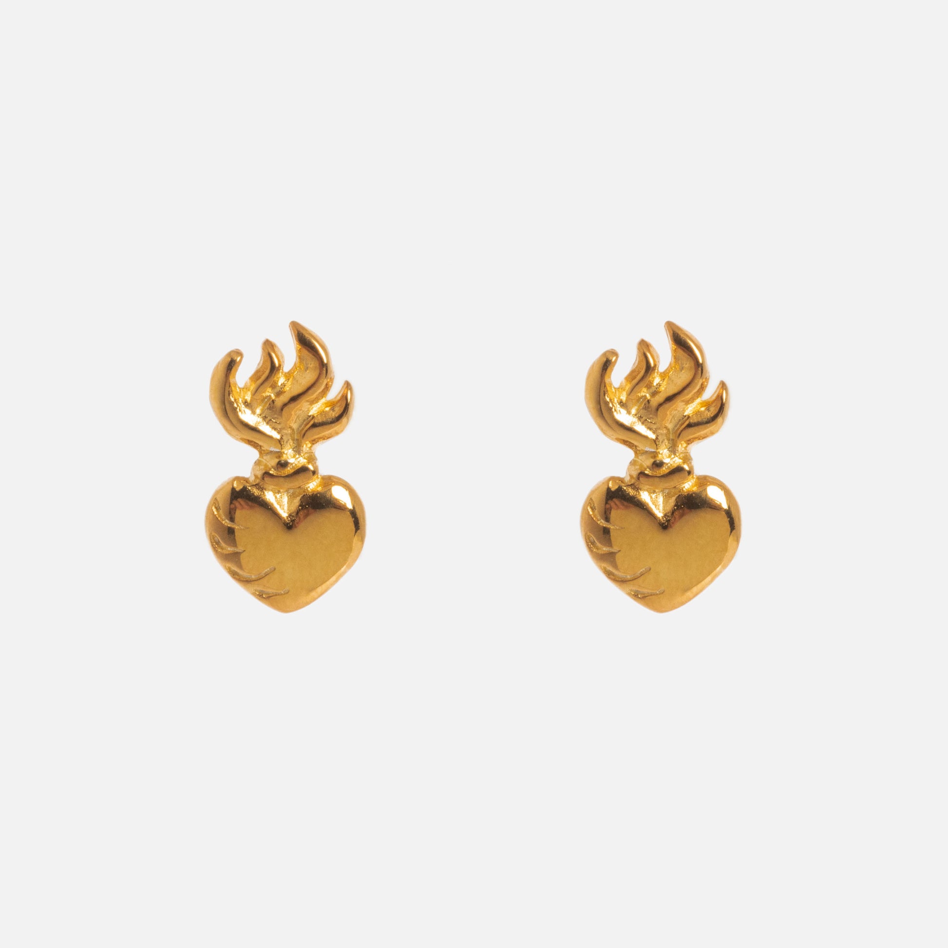 The Sacred Heart Stud Earrings are gold vermeil heart-shaped earrings with flame-like designs at the top, shown against a plain white background.