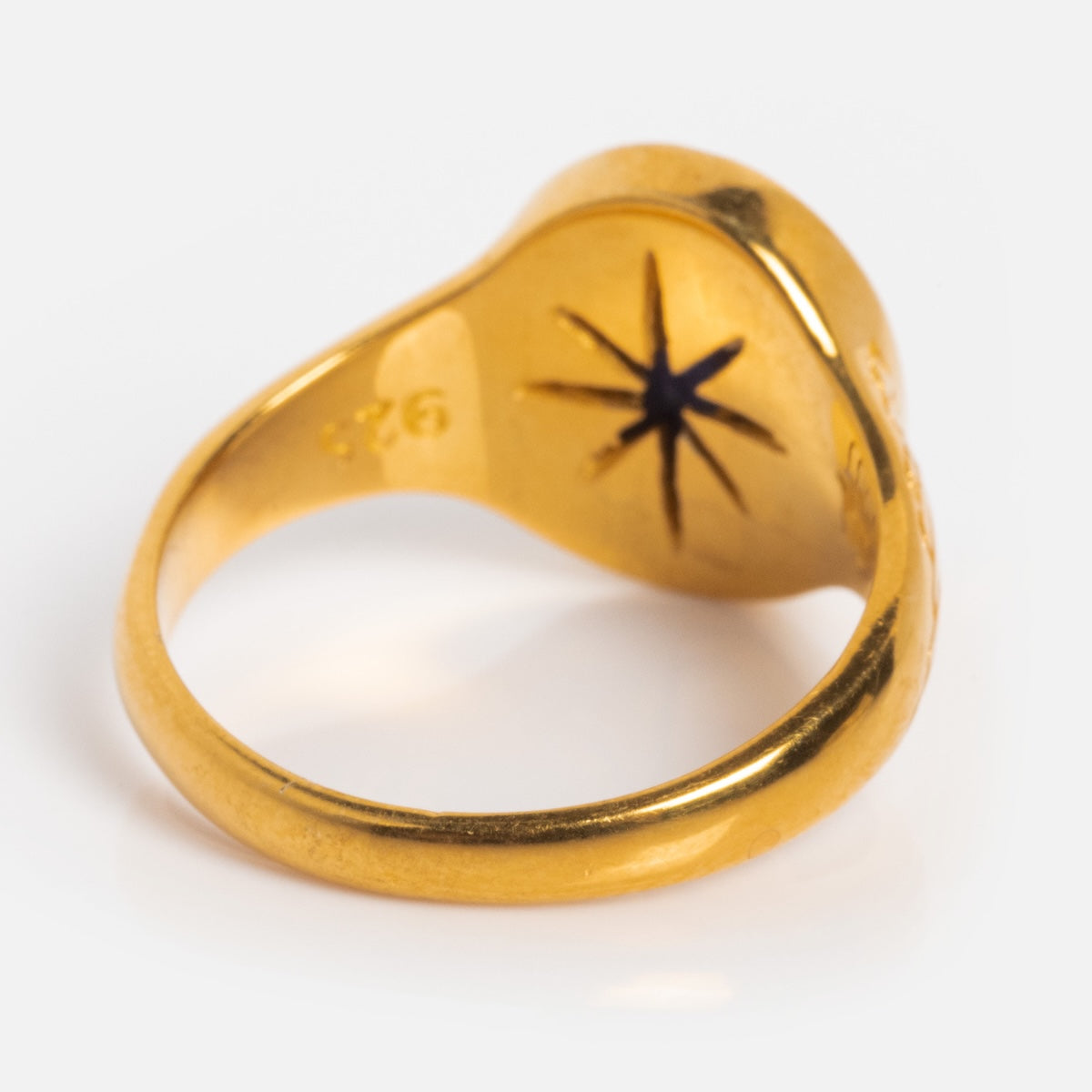 The Astral Ring is a gold vermeil piece with a smooth, rounded band. Its interior displays a black star-shaped cutout, wing engraving, and a “925” hallmark stamp.