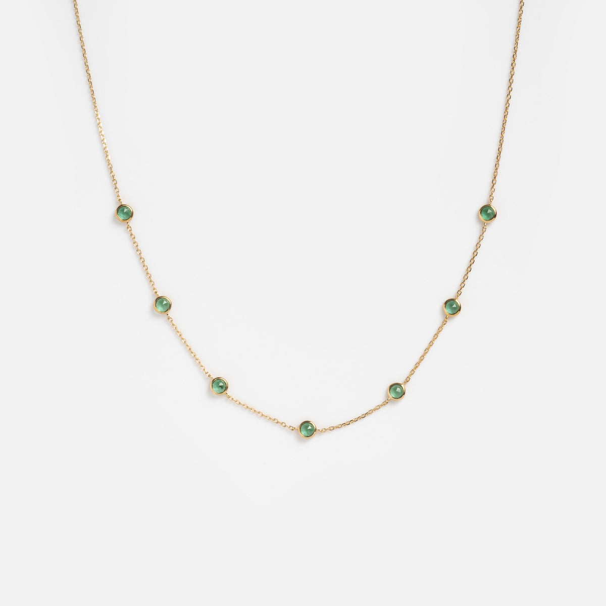 Solid Gold Birthstone Station Necklace Sample featuring seven evenly spaced green lab-created gemstones set on a 9k solid yellow gold chain, shown against a plain white background.