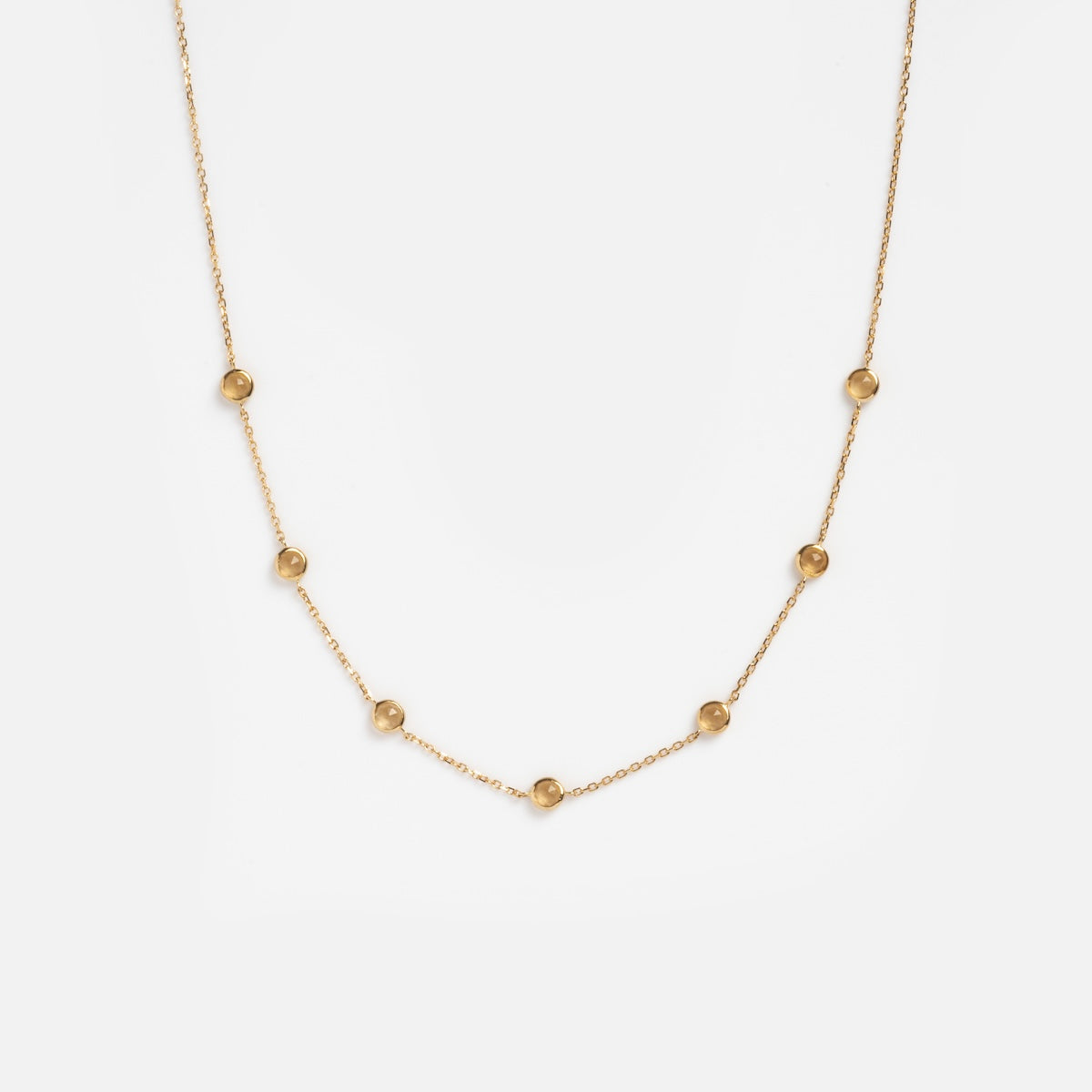 Solid Gold Birthstone Station Necklace Sample: 9k yellow gold necklace featuring seven evenly spaced small gold beads on a fine chain, shown on a plain white background.