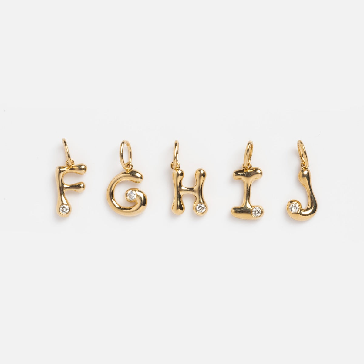 Five Solid Gold Diamond Initial Charm Samples—F, G, H, I, and J—crafted in 9k yellow gold with a 2 mm lab-created diamond at the base are displayed in a row on a white background.