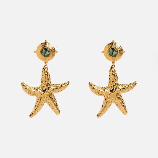 The Ebb Earrings by Petit Moments feature gold, starfish-shaped drops with textured surfaces and a round stud topped with a small iridescent stone, shown against a plain white background.