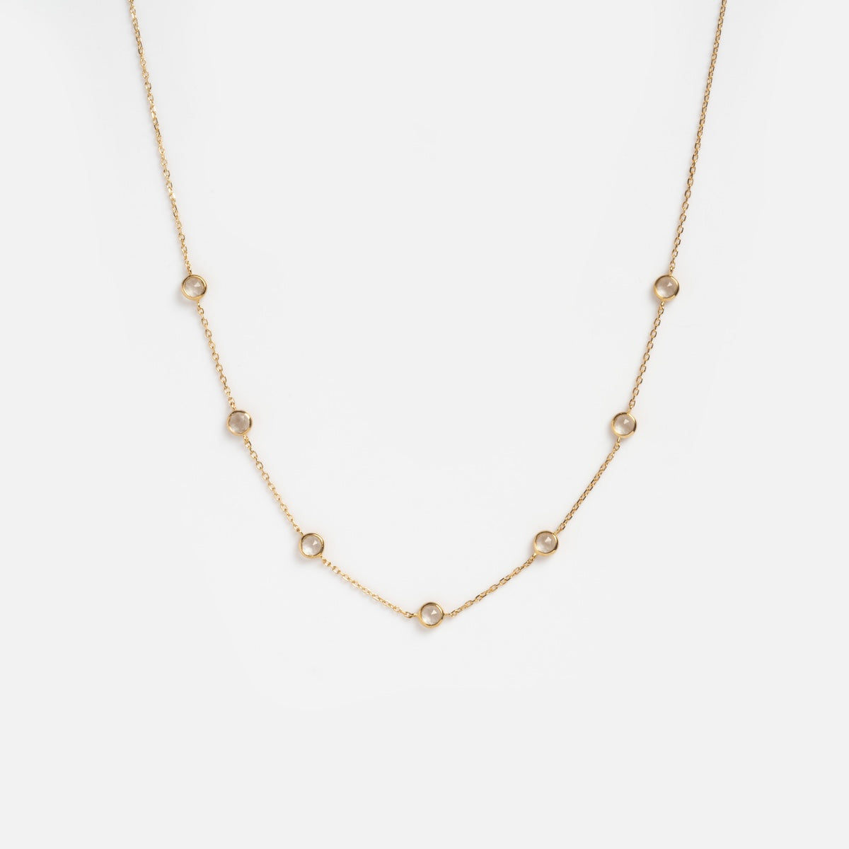 The Solid Gold Birthstone Station Necklace Sample is a delicate 9k yellow gold chain with small round bezel-set lab-created gemstones spaced evenly along the necklace, shown on a plain white background.