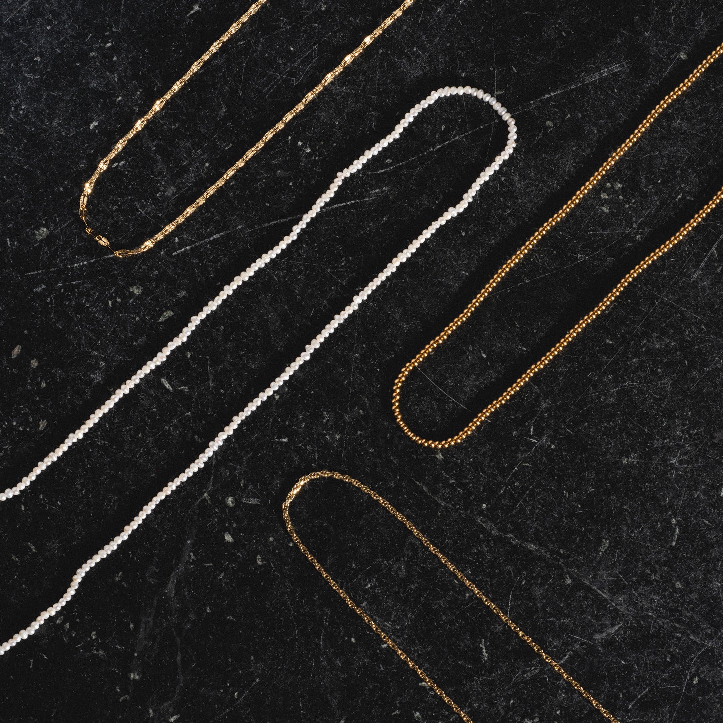 Delicate rope, beaded vermeil, pearl, and sparkle link chains arranged on black marble