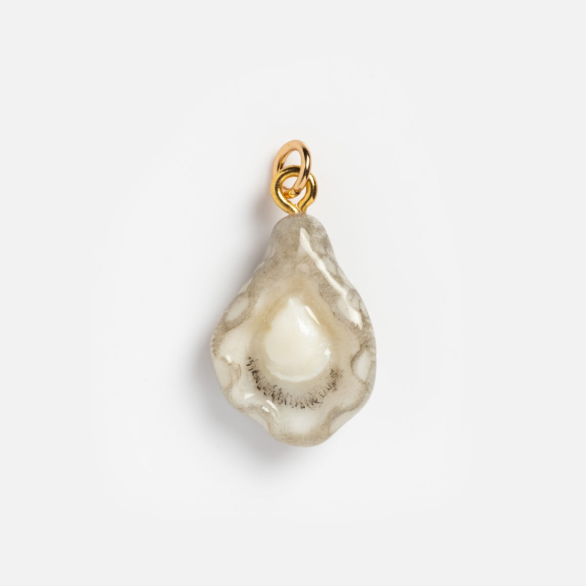 The Charms by Warm Clay Co features a hand-crafted small oyster-shaped pendant with a pearl inside, a translucent textured shell, and a gold loop. This unique charm makes an elegant necklace accent, shown on a plain white background.