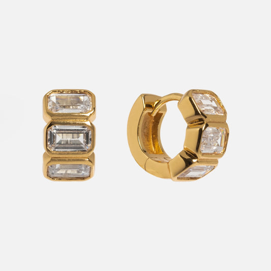 Sunset Earrings: A pair of 14k yellow gold hoops featuring three rectangular clear gemstones in a row, displayed on a plain white background.