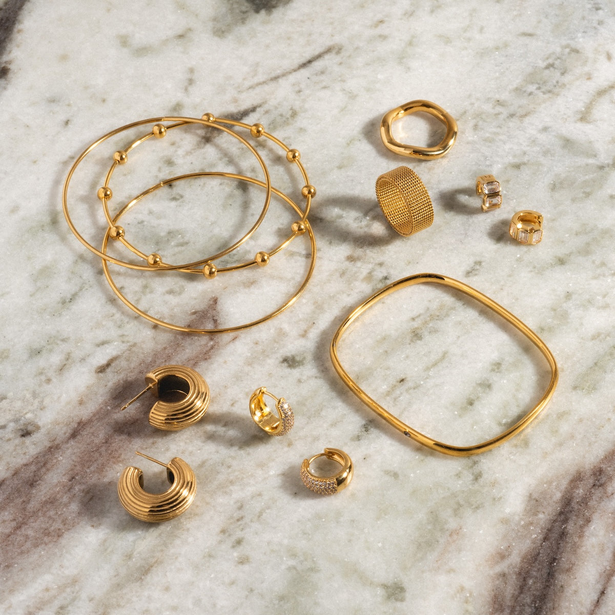 Chantel Earrings, along with 14k gold plated bangles, rings, and studs, displayed on a marble surface featuring cream, brown, and green tones.
