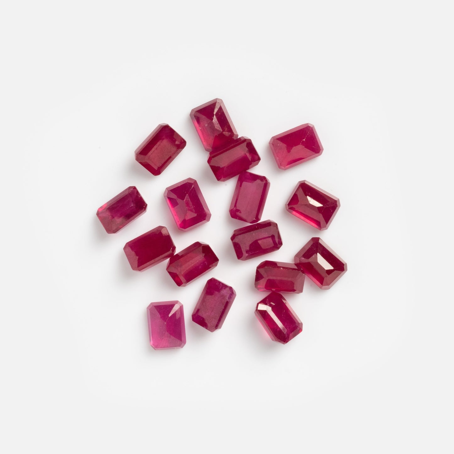 A scattered group of rectangular, faceted 2.7 carat loose ruby samples displayed on a plain white background.