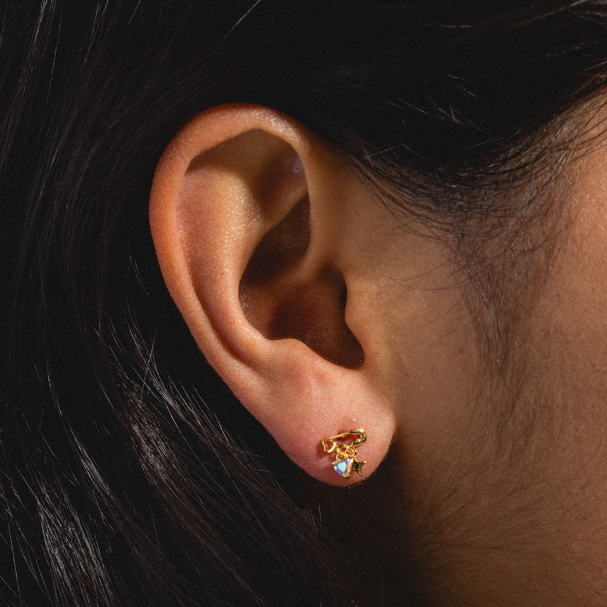 Close-up of a person with dark hair and warm-toned skin wearing Pillow Talk Dangle Earrings—18k gold plated small hoops featuring a dangling star and gemstone detail.
