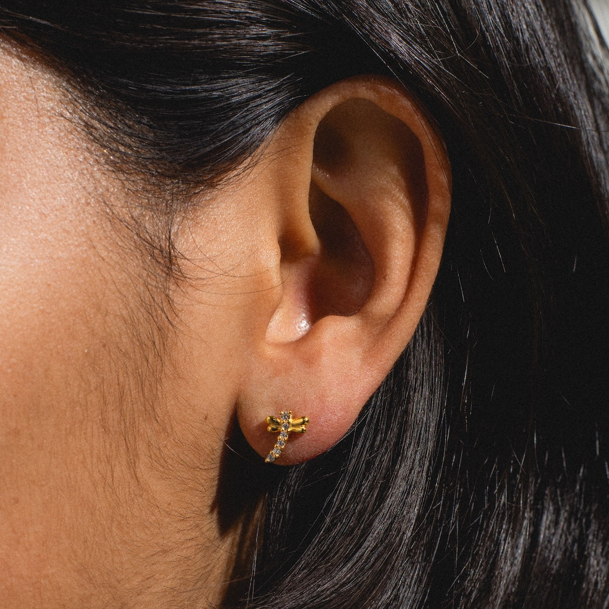 Close-up of a person’s ear wearing the Dragonfly Flat Back Stud. The softly blurred background and dark hair partially frame the ear, drawing attention to the delicate dragonfly-shaped gold vermeil earring.