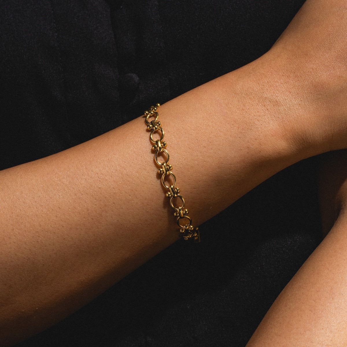 The Aubrey Bracelet, crafted in 14k gold with circular links, is worn on a model’s wrist with crossed arms against a dark backdrop, showcasing its elegant design.