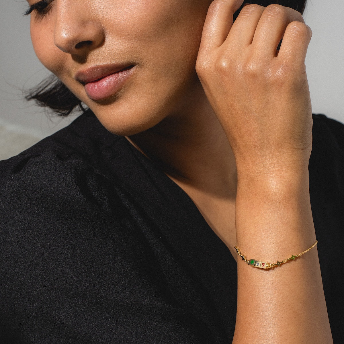 A woman in a black top rests her hand on her face, highlighting her lower face, neck, and arm while wearing the Hit The Jackpot Bracelet—a stylish piece embellished with colorful gemstones.