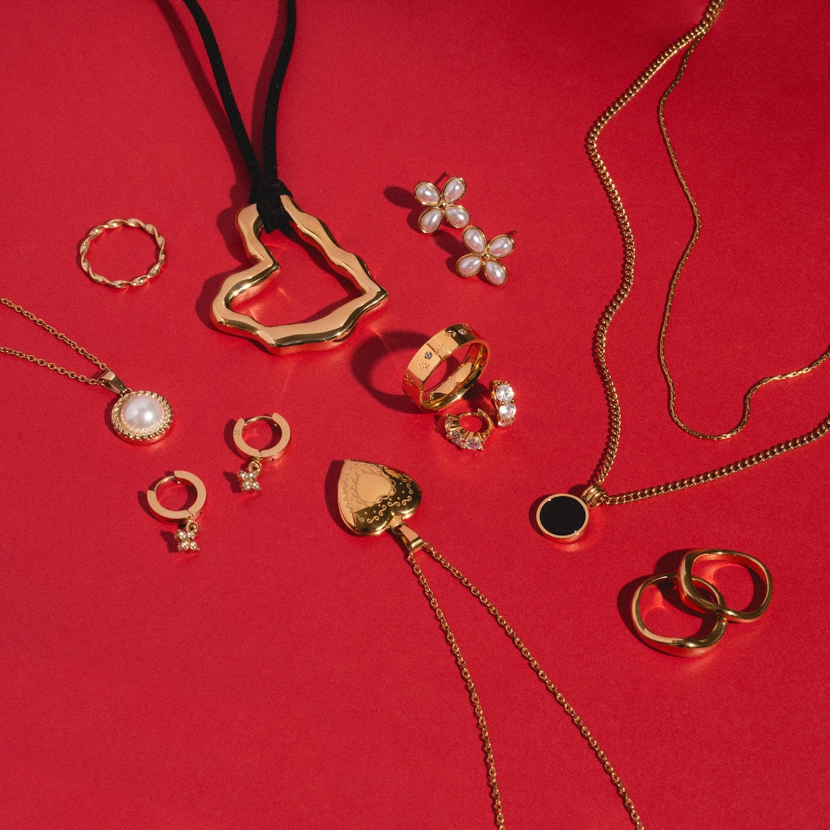 Merveilles Hoops, stunning CZ yellow gold earrings with pearl and gemstone accents, are displayed on a vibrant red background.