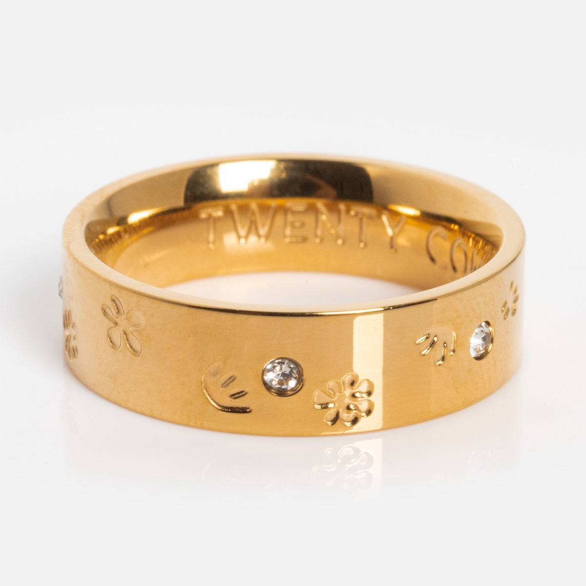 The Work of Art Ring is a yellow gold plated CZ ring with an engraved band, featuring small flower and smiley face designs spaced between clear gemstones, shown on a white background.