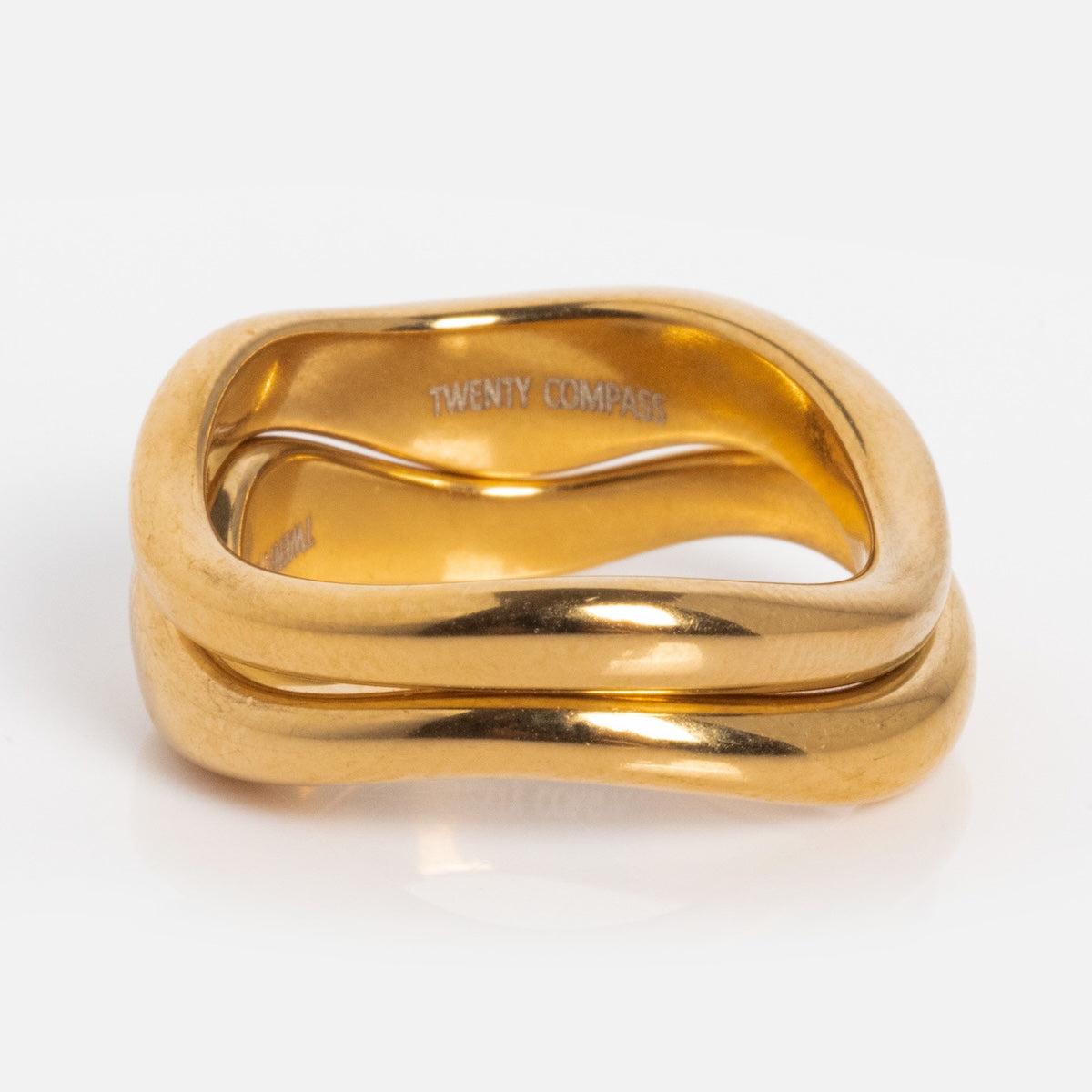 The Curves Ring Set features two stacked, wavy gold plated rings with a polished finish and TWENTY COMPASS engraved inside the top ring, beautifully presented on a white background.