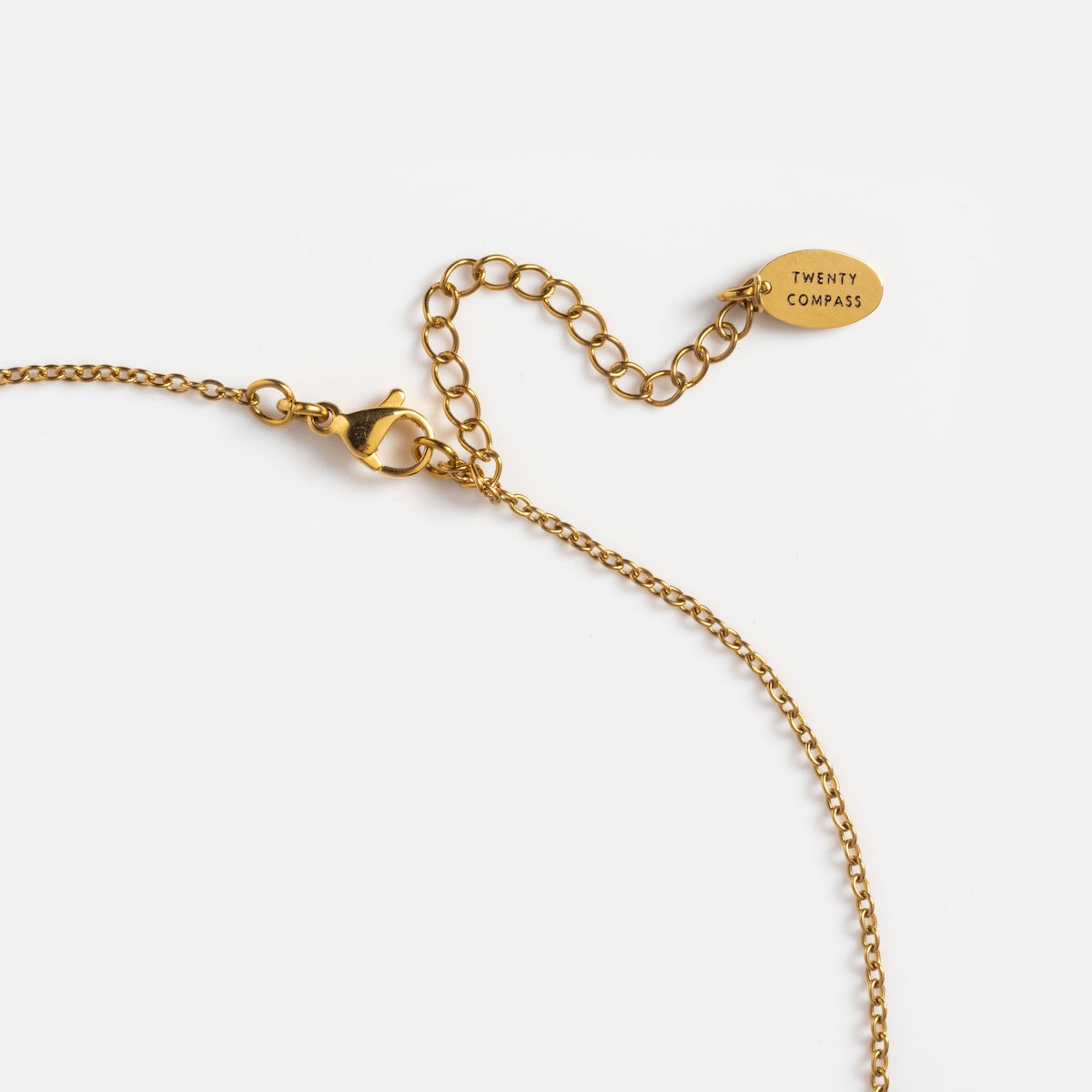 The Paloma Necklace is a delicate yellow gold plated piece with a lobster clasp, extender, and an oval tag engraved with TWENTY COMPASS, shown on a white background.