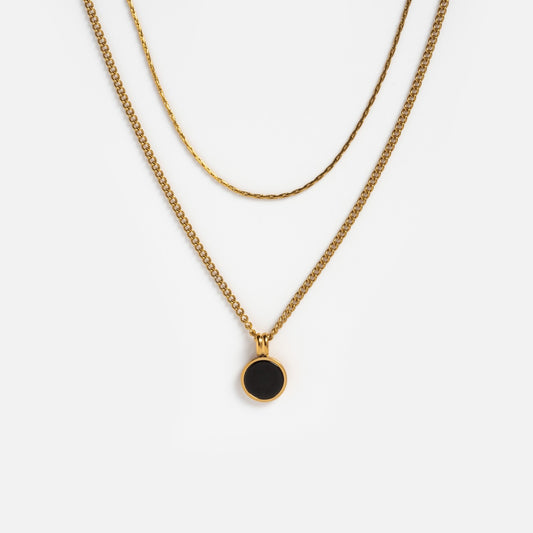 Two gold necklaces are shown on a white background: one is the Billie Necklace chain, and the other has a small round black coin pendant in gold, creating an elegant layered necklace style.