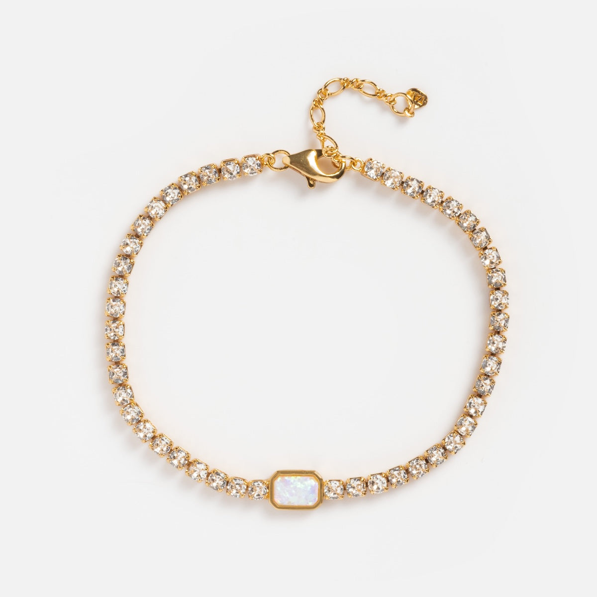 The Tennis Bracelet with Opal features a 14k gold plated chain, a central opal, clear round-cut gemstones surrounding the opal, an adjustable chain, and clasp, all displayed on a white background.