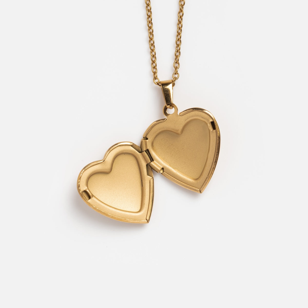 The Daydream Necklace showcases a gold heart locket on a fine gold chain, opening to reveal two empty spaces inside, displayed on a plain white background.