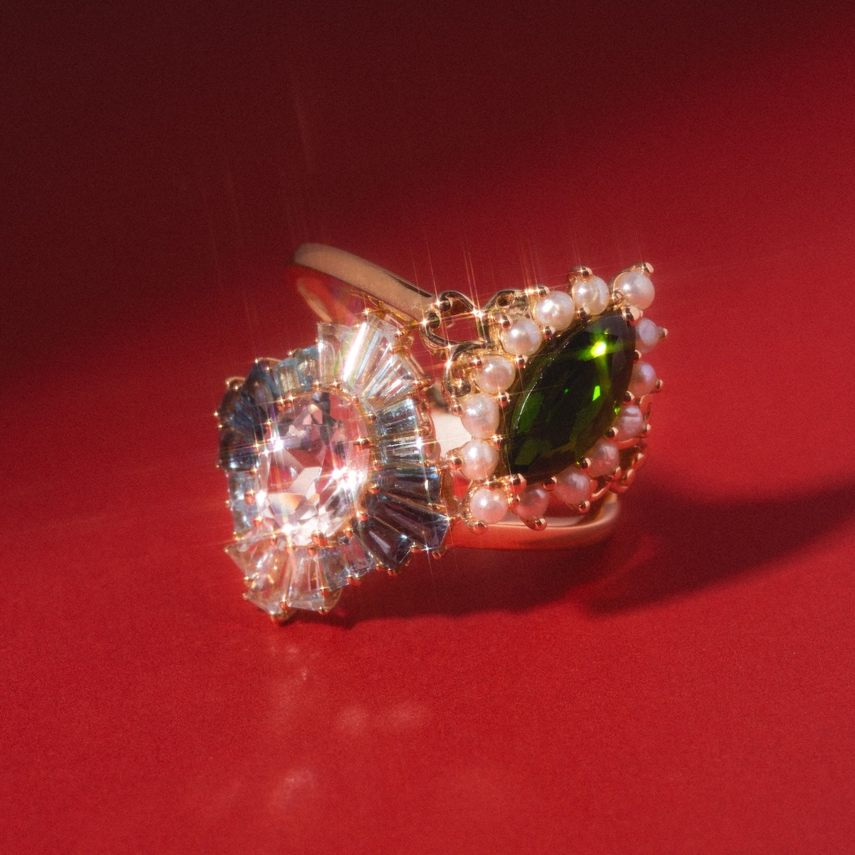 The 14k Opulent Green Diopside and Pearl Marquise Ring showcases a striking marquise green diopside and lustrous pearls, beautifully highlighted on a red background with dramatic lighting.