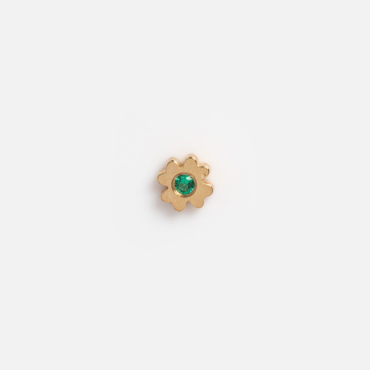 A solid gold tiny lucky charm for glass charm locket, shaped like a six-petal flower with a green gemstone center, reminiscent of gold good luck charms, shown on a plain white background.