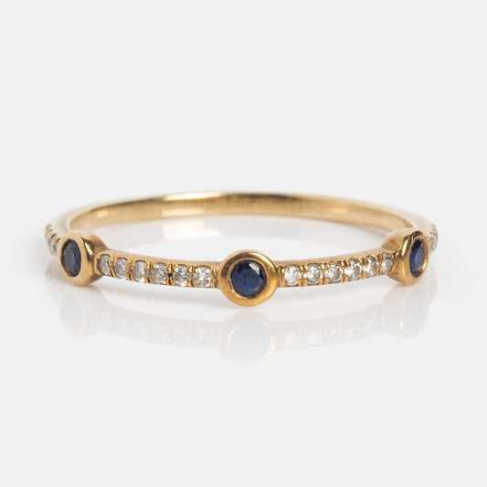 The Solid Gold Slim Sapphire and Diamond Stacking Ring features three round blue sapphires with sparkling diamonds set between them on a delicate gold band, shown against a white background.