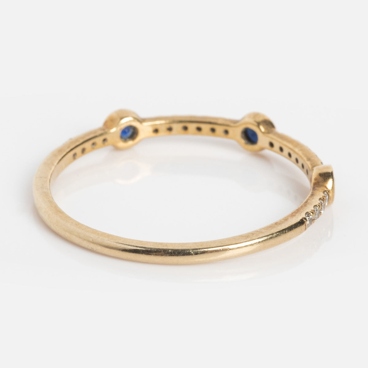 The Solid Gold Slim Sapphire and Diamond Stacking Ring features a delicate gold band adorned with spaced blue sapphires and a cluster of tiny clear diamonds for a subtle, sparkling touch.