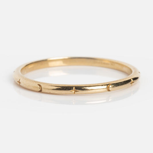 The Solid Gold Delicate Celestial Stacking Ring is a thin gold band engraved with small star patterns evenly spaced around it, perfect for layering.